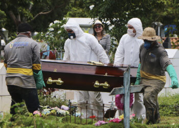 A relative stands at a distance during the burial of Robson de Souza Lopes at Parque Taruma cemetery in Manaus, Brazil, Tuesday, March 31, 2020. According to authorities at the Amazonas Health Secretary, the 43-year-old musician died Monday after being diagnosed with COVID-19. (AP Photo/Edmar Barros)