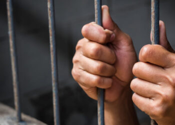 Soft focus on hands of man behind jail bars. vintage or retro style. selective focus.